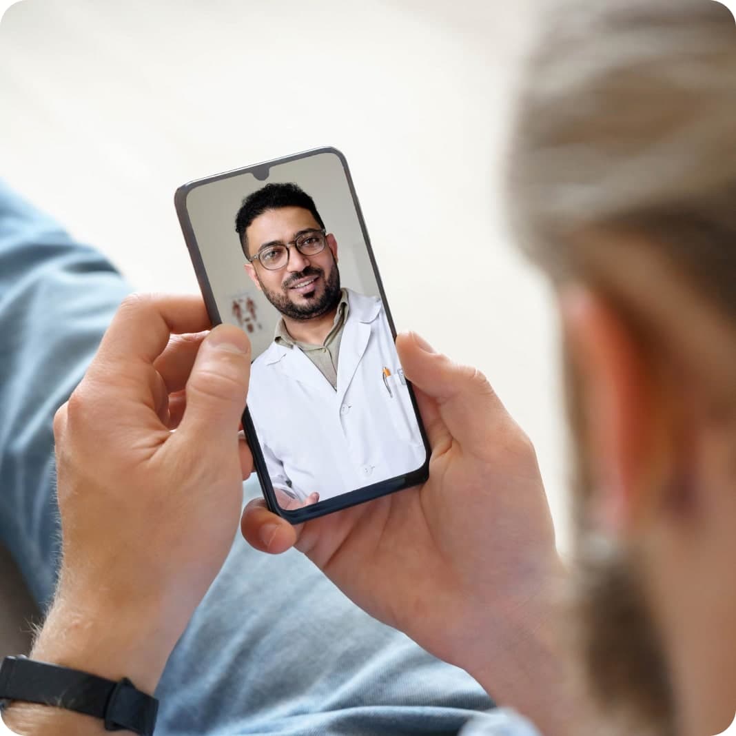 Person holding a smartphone showing a video call with a man wearing glasses and a white coat, smiling at the camera.