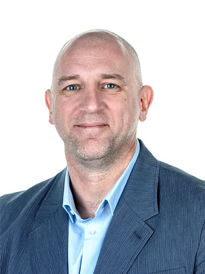A bald man in a blue blazer and light blue shirt smiles against a plain white background.
