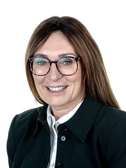 Woman with long brown hair, wearing glasses, a black jacket, and a white blouse, smiling