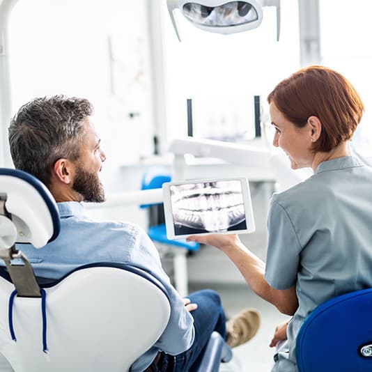 Dentist showing a dental X-ray on a tablet to a male patient sitting in a dental chair.