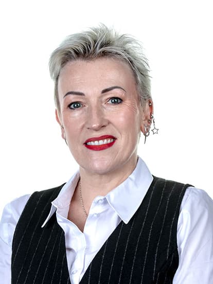 Smiling person with short hair, wearing a white shirt and black vest