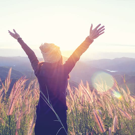 Lady standing in a field with arms raised towards the sunrise