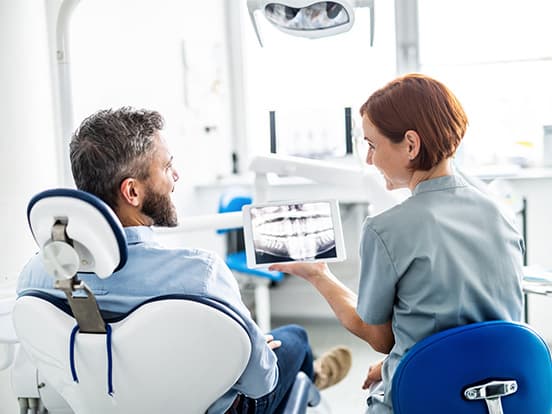 A dentist shows a patient dental X-rays on a tablet in a modern dental office.