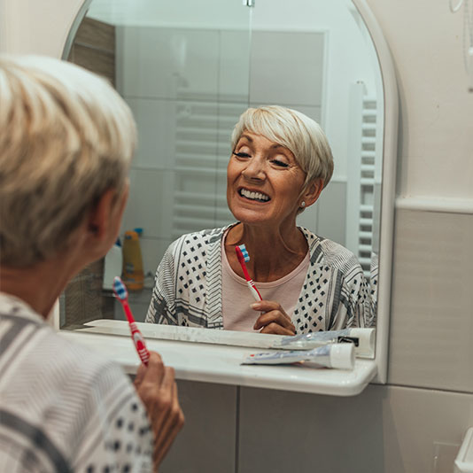 Lady brushing her teeth in bathroom mirror