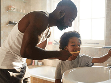 Father helping young son brush their teeth